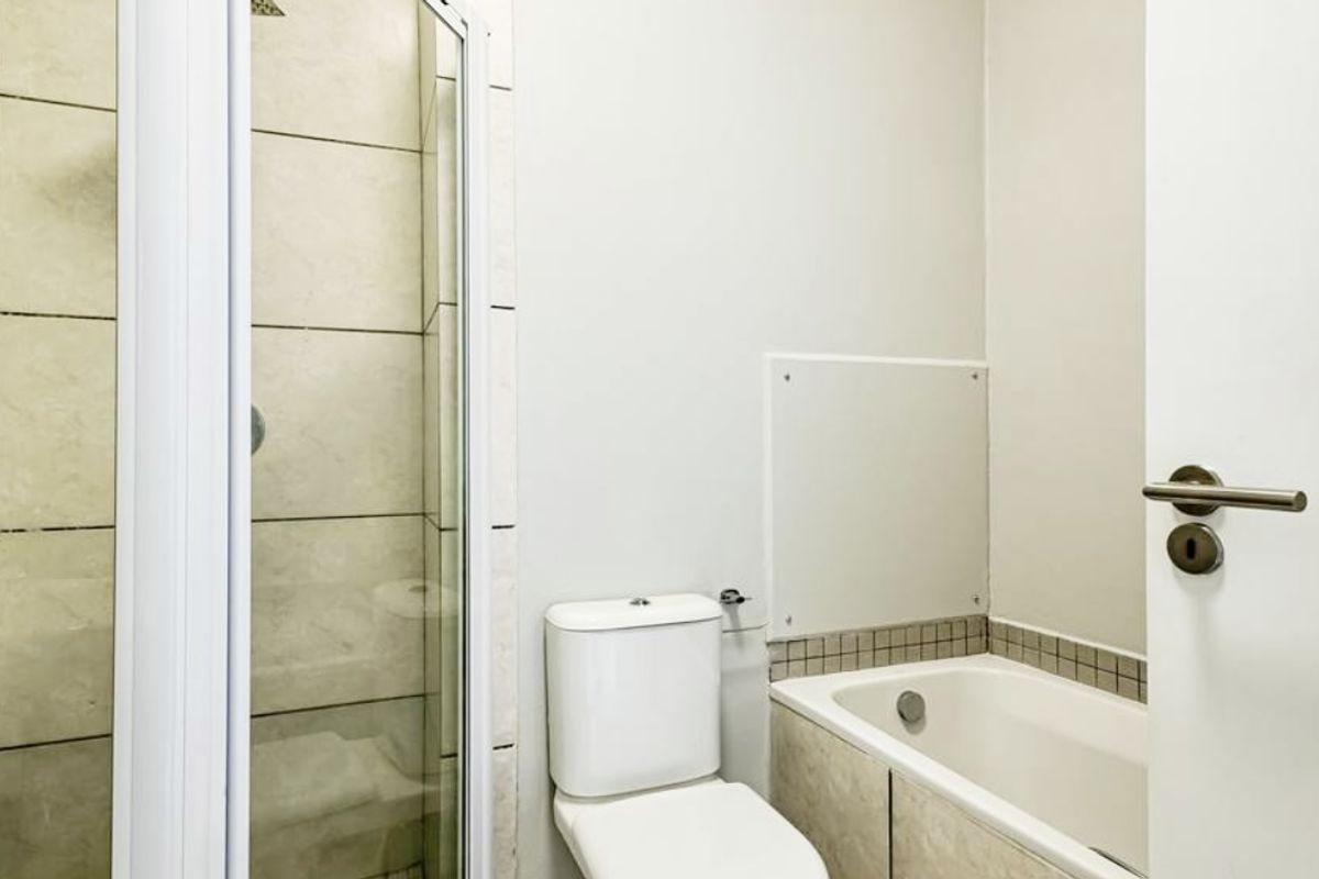 A functional bathroom featuring a glass-enclosed shower, a built-in bathtub with tiled surround, and a standard toilet.