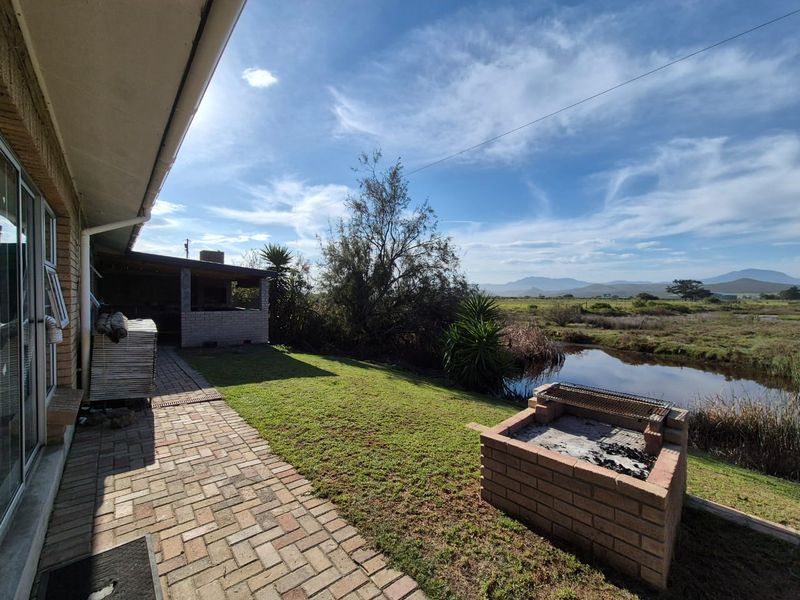 Rear exterior view featuring a brick paved patio, built-in braai area, landscaped garden, and scenic water views.