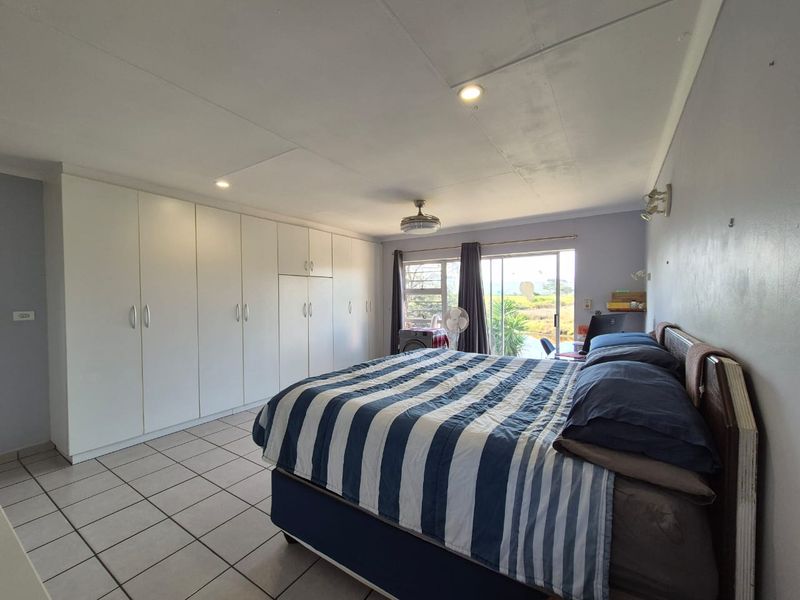 Spacious bedroom featuring extensive built-in cupboards, tiled flooring, a ceiling fan, and sliding glass doors providing natural light and outdoor access.