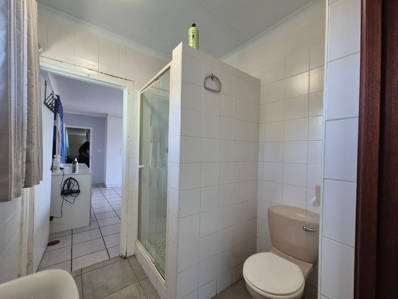 A functional bathroom featuring a shower enclosure, toilet, and tiled finishes, currently showing signs of age and wear.