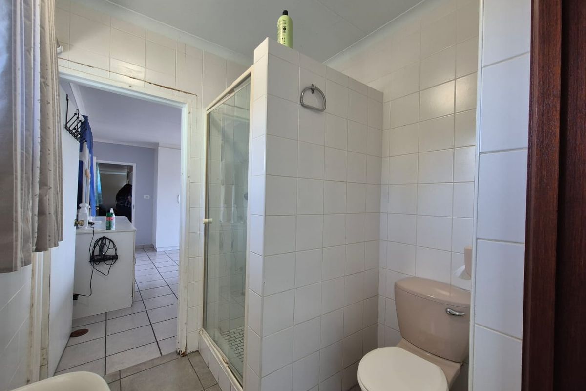 A functional bathroom featuring a shower enclosure, toilet, and tiled finishes, currently showing signs of age and wear.