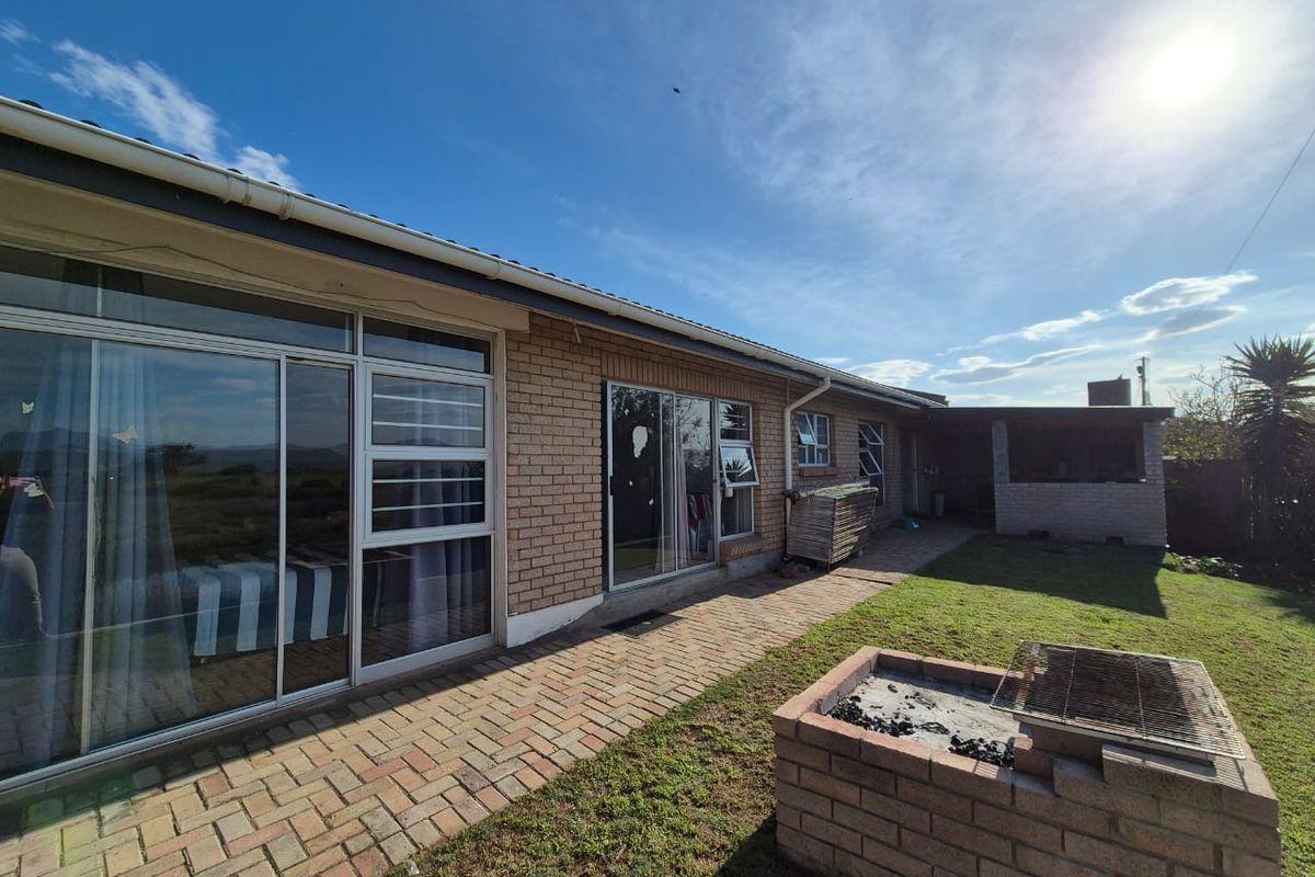 Rear exterior view featuring a brick facade, sliding glass doors, paved patio area, and a built-in brick braai in the garden.
