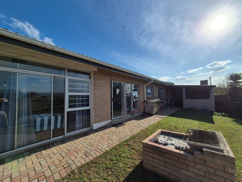 Rear exterior view featuring a brick facade, sliding glass doors, paved patio area, and a built-in brick braai in the garden.