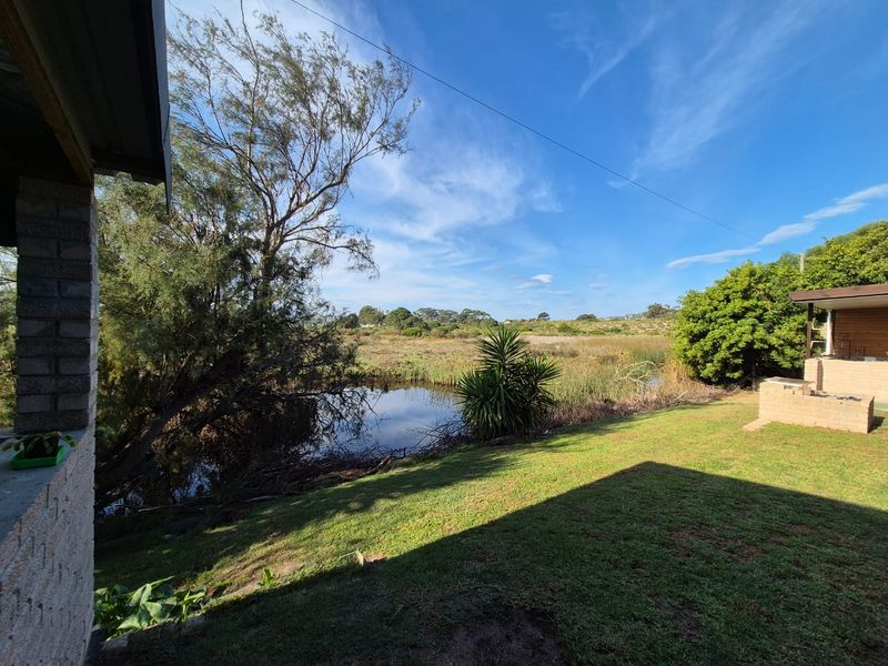 A scenic view of the natural wetland area from the backyard, featuring a built-in brick braai and established garden space.