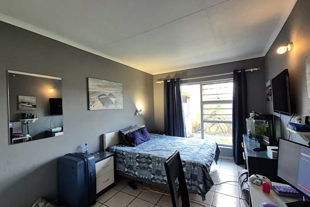 A functional bedroom featuring tiled flooring, neutral grey walls, and a sliding window providing natural light.