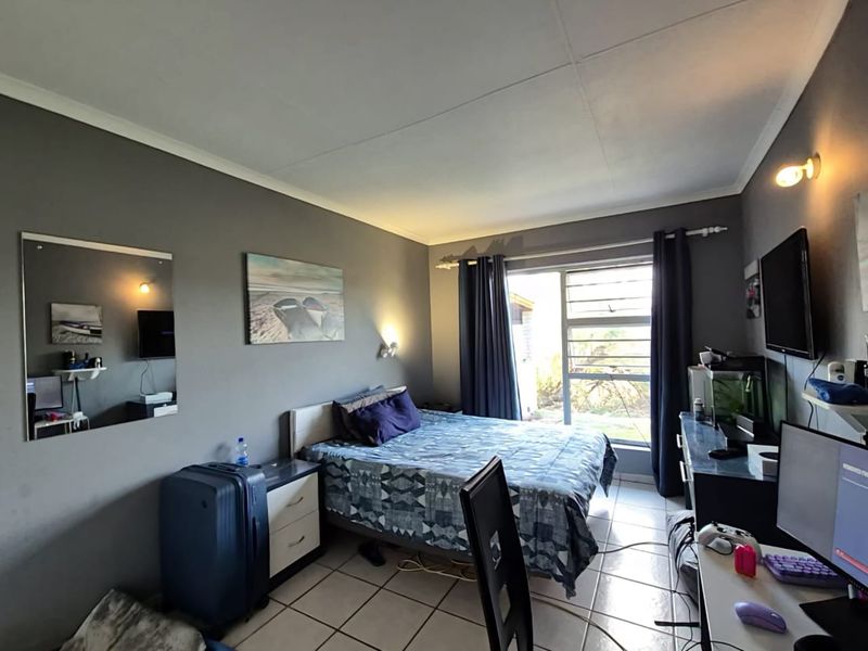 A functional bedroom featuring tiled flooring, neutral grey walls, and a sliding window providing natural light.