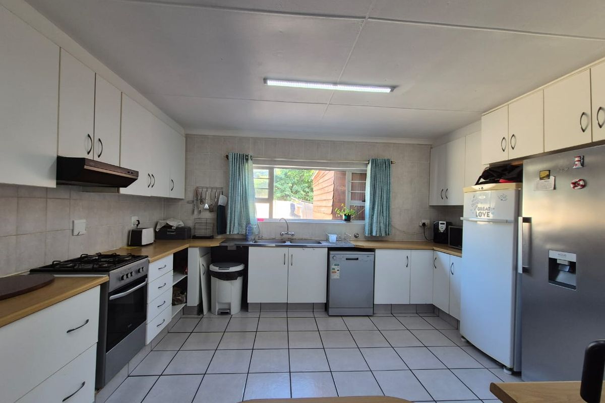 A functional kitchen featuring white cabinetry, tiled flooring, a gas stove with extractor fan, and a double basin sink under a window.