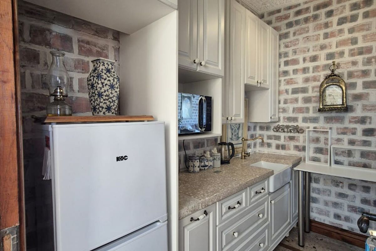 A charming kitchen featuring exposed brick walls, white cabinetry, a farmhouse-style sink, and a unique tiled floor with decorative borders.