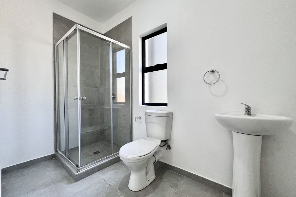 A modern bathroom featuring a glass-enclosed shower, pedestal basin, and toilet with neutral grey floor and wall tiling.