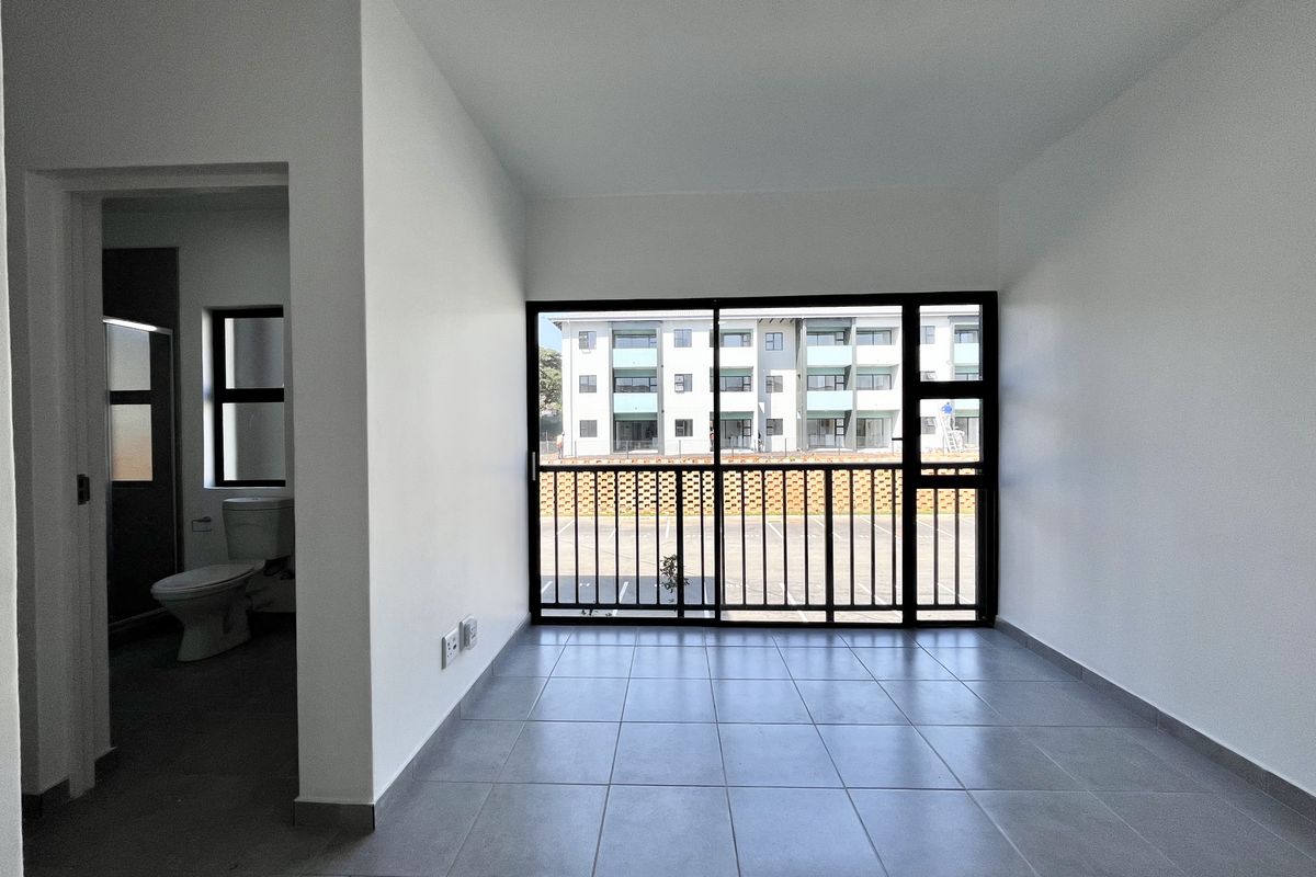 A bright, empty living area featuring neutral floor tiles, large sliding glass doors with security bars, and an adjacent bathroom.