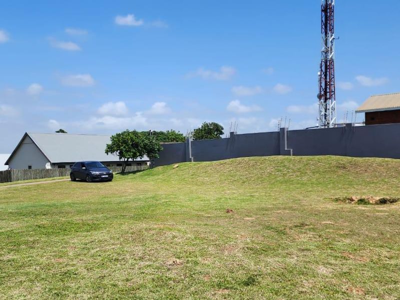 A spacious, gently sloping vacant residential plot featuring a well-maintained lawn, enclosed by a perimeter wall with electric fencing.