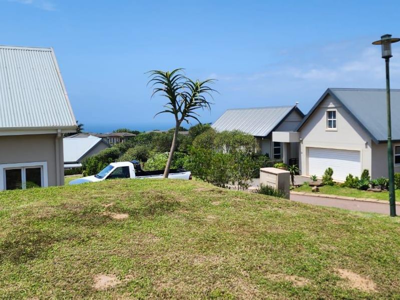 A view of a residential street featuring well-maintained homes, paved driveways, and landscaped lawns in a coastal estate setting.
