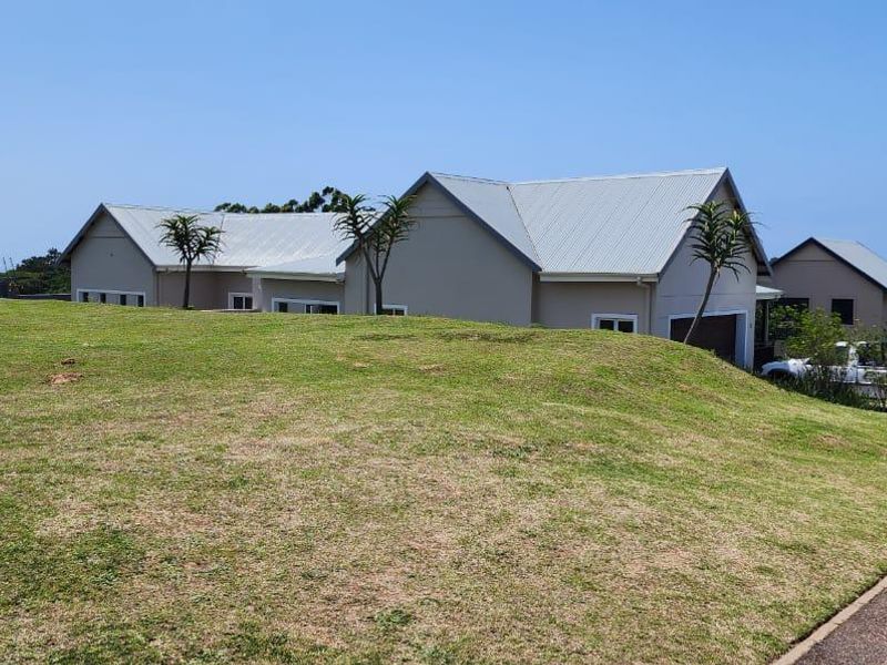 A view of a modern residential property featuring a pitched metal roof, well-maintained lawn, and paved driveway access.