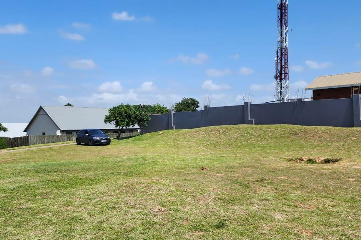 A spacious, gently sloping vacant residential plot featuring a well-maintained lawn, enclosed by a perimeter wall with electric fencing.