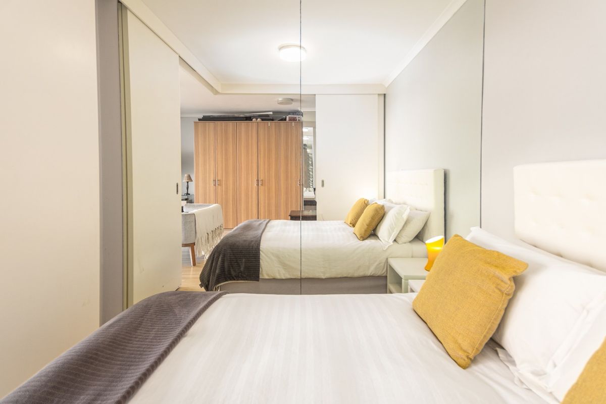 A bedroom featuring built-in wardrobes with sliding doors and a large mirrored wall panel, creating a spacious feel.