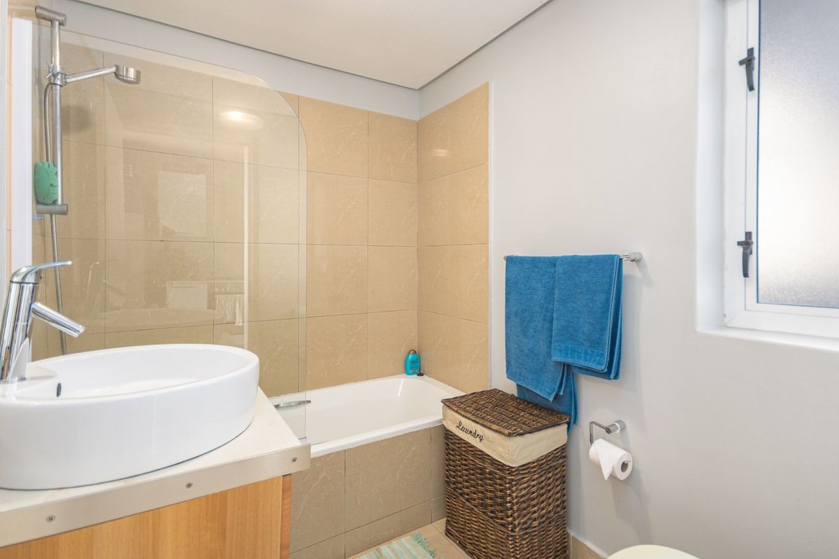 A functional bathroom featuring a built-in bathtub with a glass shower screen, a modern vessel sink vanity, and neutral wall tiling.