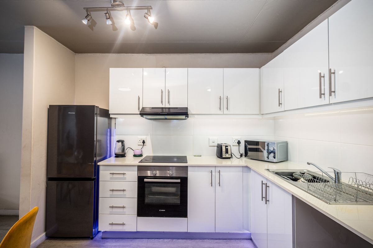 Modern kitchen featuring white high-gloss cabinetry, integrated oven, electric hob, extractor fan, and a stainless steel sink with tiled splashbacks.