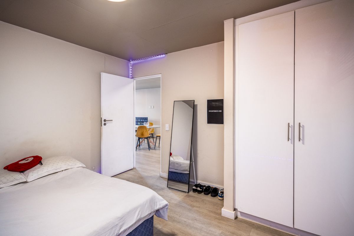 A bedroom featuring built-in white cabinetry and light-toned flooring, with a doorway leading to an adjacent living area.