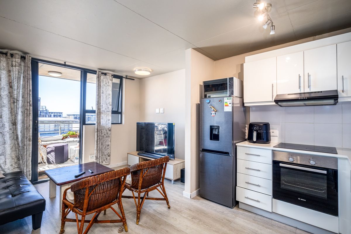 Open-plan living area featuring a modern kitchen with built-in oven, hob, and extractor fan, leading to a balcony with urban views.