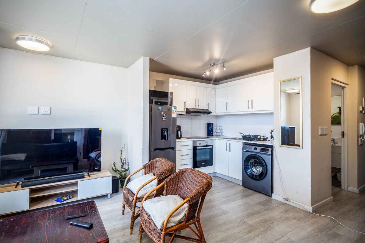 Open-plan living area featuring a modern kitchen with white cabinetry, integrated oven, hob, extractor fan, and space for a washing machine.