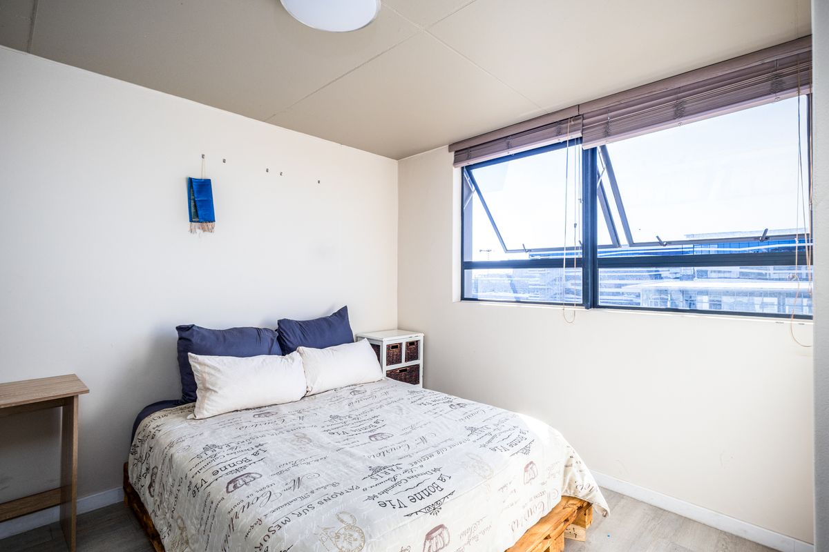 A functional bedroom featuring a large window with integrated blinds, neutral wall finishes, and light-toned flooring.