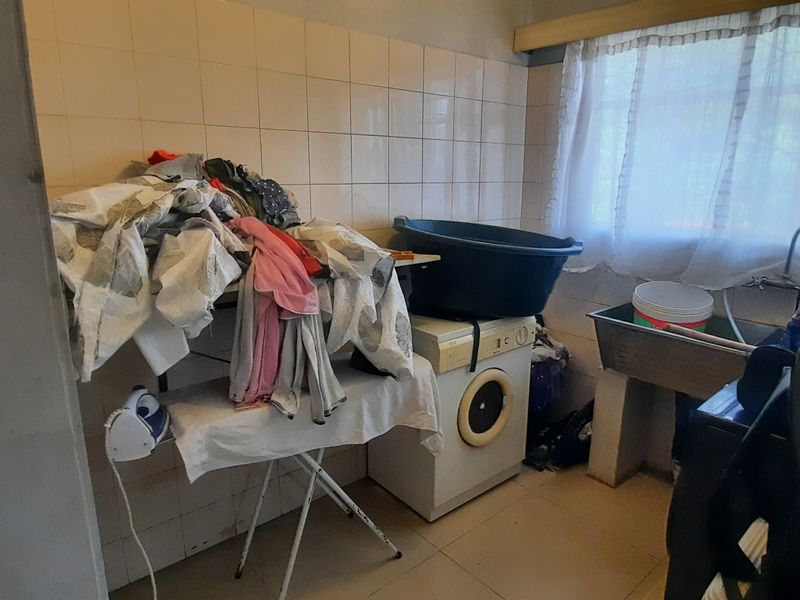 A functional laundry room featuring tiled walls, a stainless steel utility sink, and space for laundry appliances.