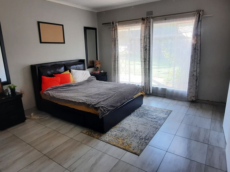 Spacious bedroom featuring tiled flooring, built-in wardrobe storage, and a large sliding glass door providing natural light and garden access.