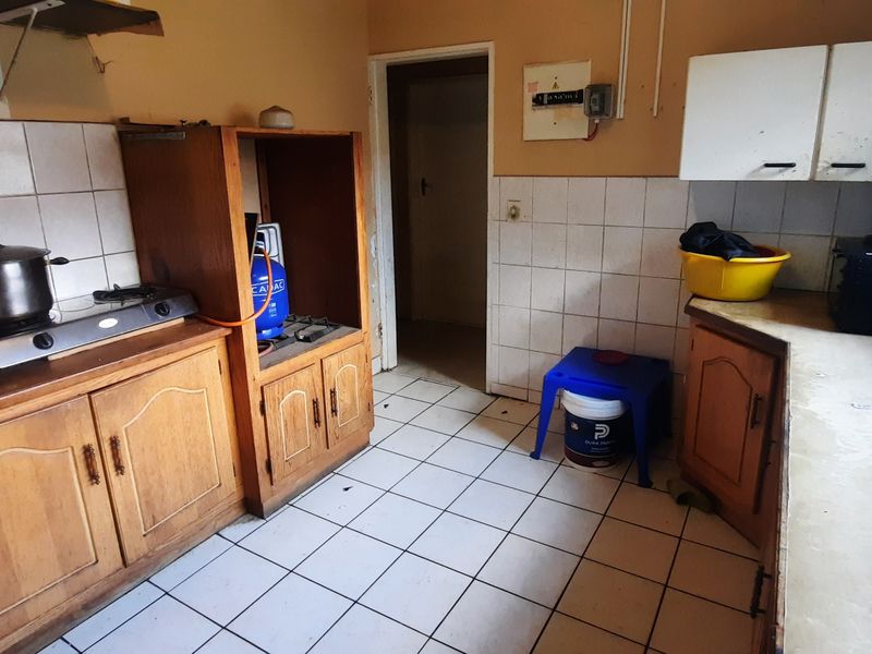 A dated kitchen featuring wooden cabinetry, tiled splashbacks, and tiled flooring, offering significant potential for modernization and renovation.