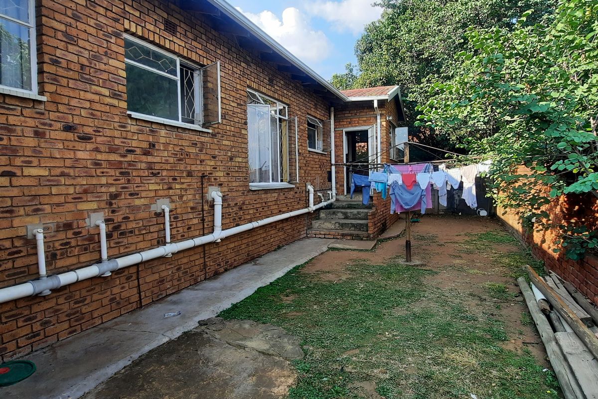 Rear exterior view of the property featuring exposed brick walls, external plumbing lines, a concrete pathway, and a private garden area.