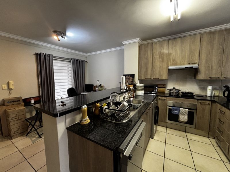 Open-plan kitchen featuring wood-look cabinetry, granite countertops, built-in oven, hob, and extractor fan, seamlessly flowing into the adjacent living area.