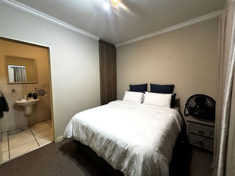A bedroom featuring built-in wooden cabinetry and an en-suite bathroom with tiled flooring and a wall-mounted basin.
