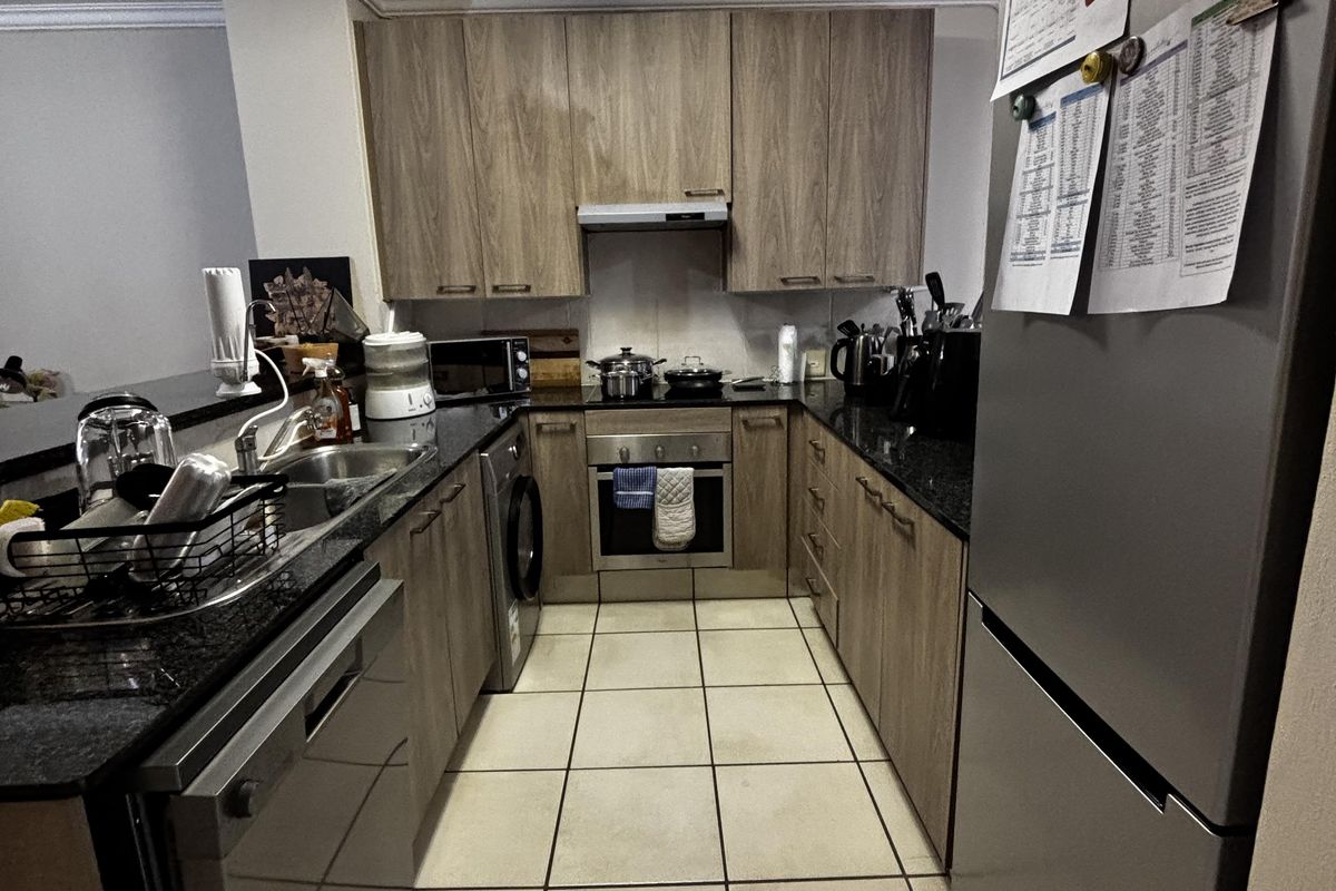 A functional galley-style kitchen featuring wood-look cabinetry, dark granite countertops, integrated oven, and tiled flooring.