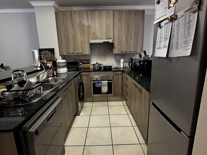 A functional galley-style kitchen featuring wood-look cabinetry, dark granite countertops, integrated oven, and tiled flooring.