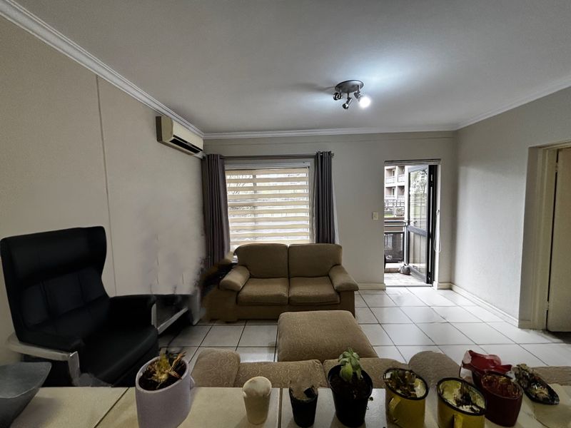 A living room featuring tiled flooring, crown molding, a wall-mounted air conditioning unit, and direct access to an outdoor balcony area.