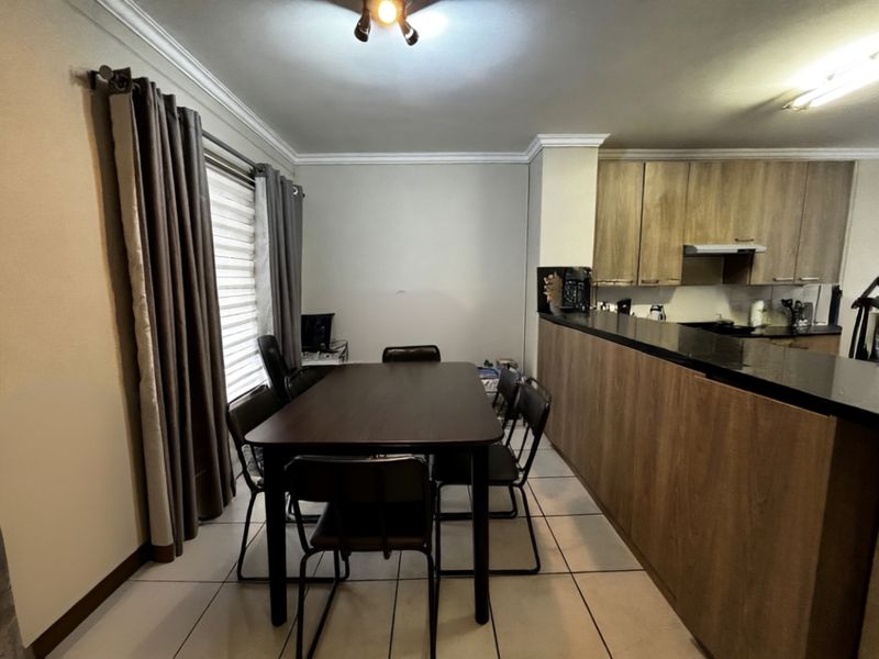 Open plan dining area adjacent to a kitchen featuring wood-look cabinetry, dark granite countertops, and tiled flooring.