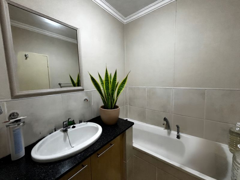 A functional bathroom featuring a built-in vanity with a granite countertop, integrated basin, and a standard bathtub with wall-mounted fixtures.
