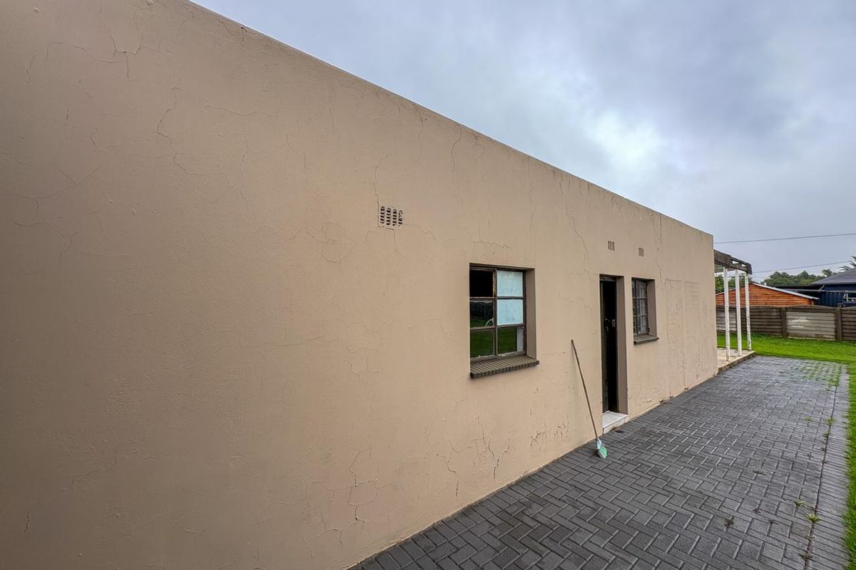 Exterior view of the rear building facade featuring paved walkway, brick wall construction, and window access.