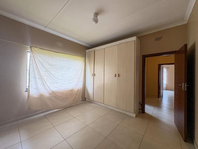 A bedroom featuring neutral floor tiles and a built-in wardrobe with light wood-finish doors.