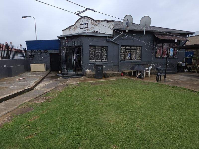 Rear view of the property featuring a paved courtyard, small lawn area, and a dark-painted exterior facade with security bars on windows.