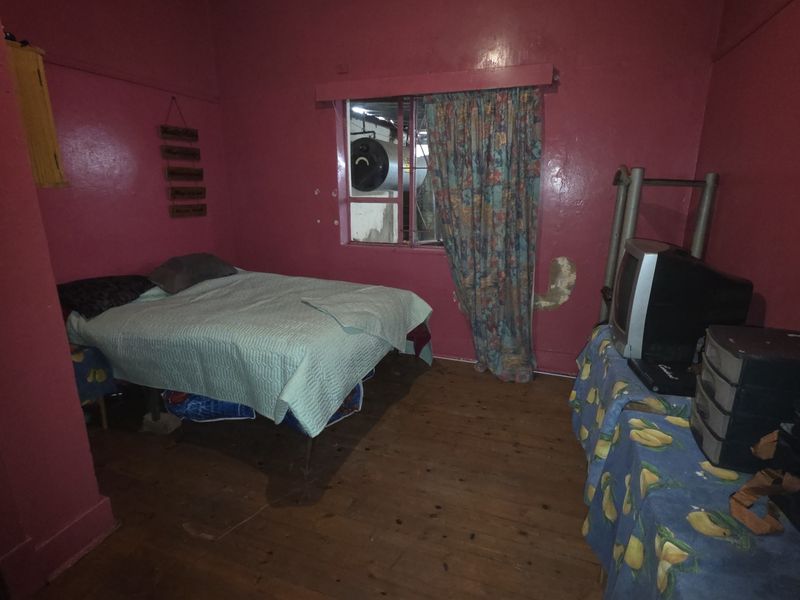 A bedroom featuring timber flooring and red painted walls, requiring cosmetic updates and repairs to the wall finishes.