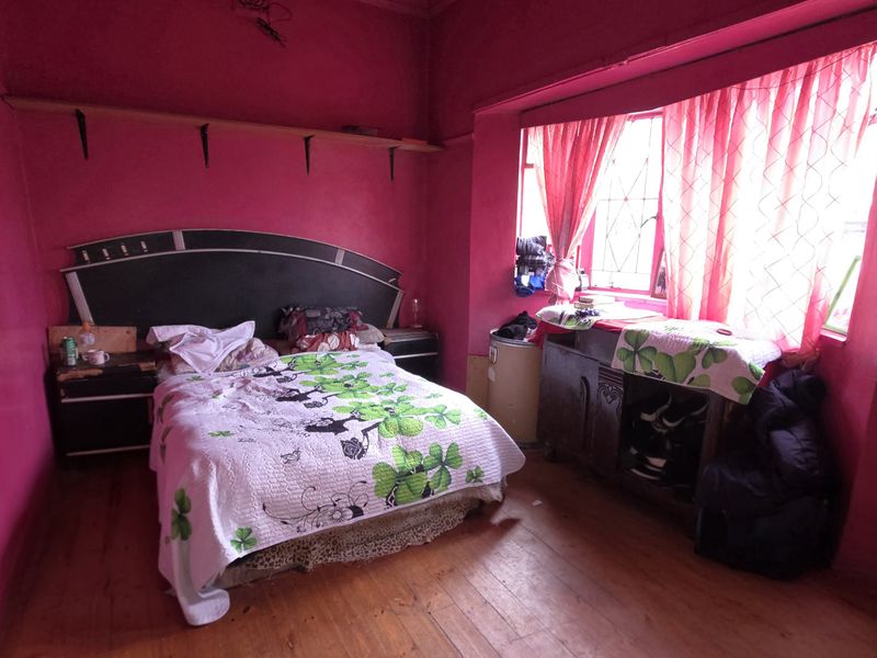 A bedroom featuring timber flooring and a large window, currently finished with bold wall coloring.