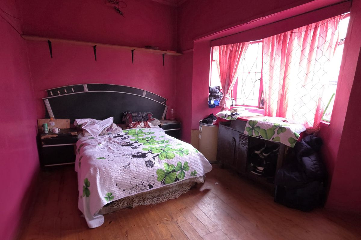 A bedroom featuring timber flooring and a large window, currently finished with bold wall coloring.