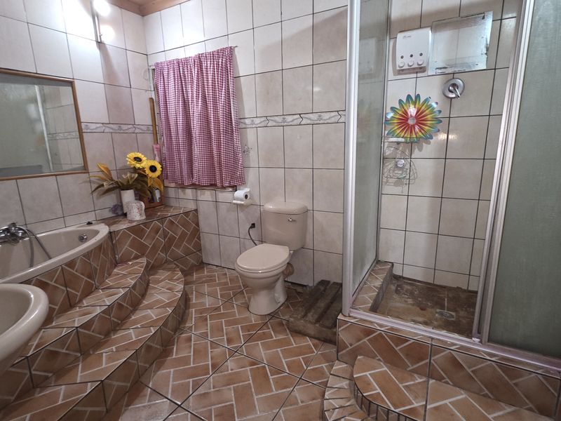 A dated bathroom featuring a raised corner bathtub, a separate shower enclosure, a pedestal basin, and a toilet with tiled flooring and walls.