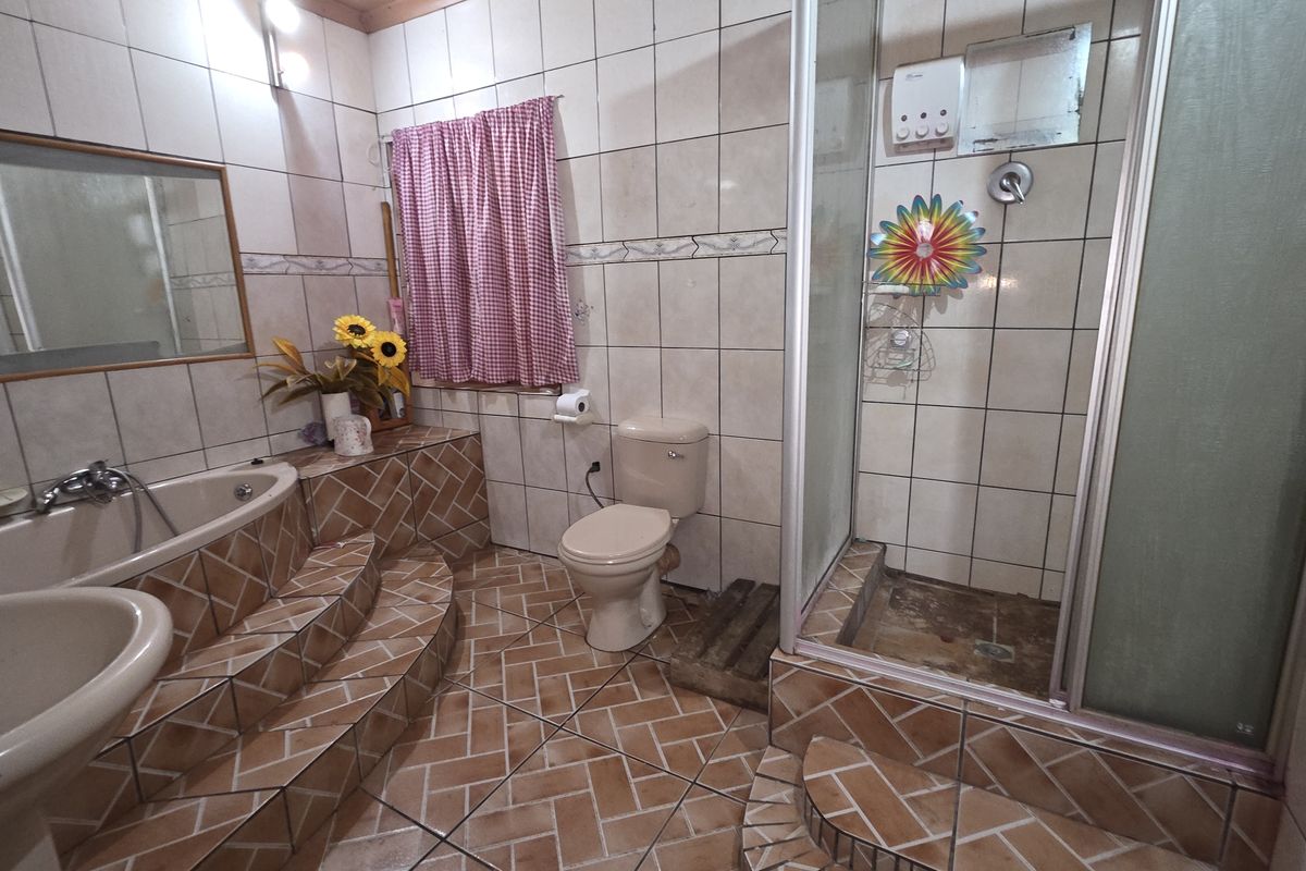 A dated bathroom featuring a raised corner bathtub, a separate shower enclosure, a pedestal basin, and a toilet with tiled flooring and walls.