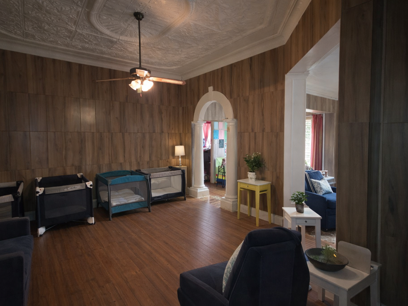 Spacious living area featuring ornate pressed metal ceilings, timber wall paneling, and a classic arched doorway leading to an adjoining room.