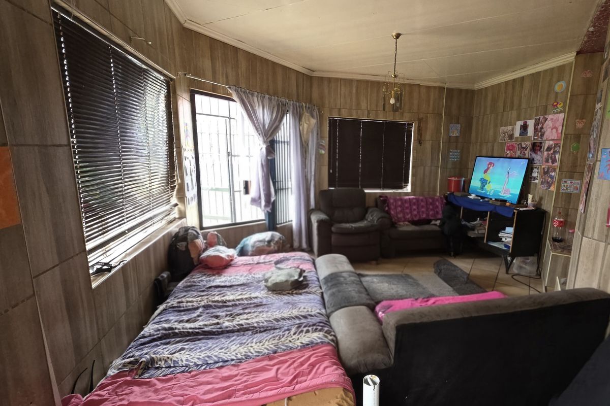 A living room featuring wood-look wall paneling, tiled flooring, and security bars on the windows.