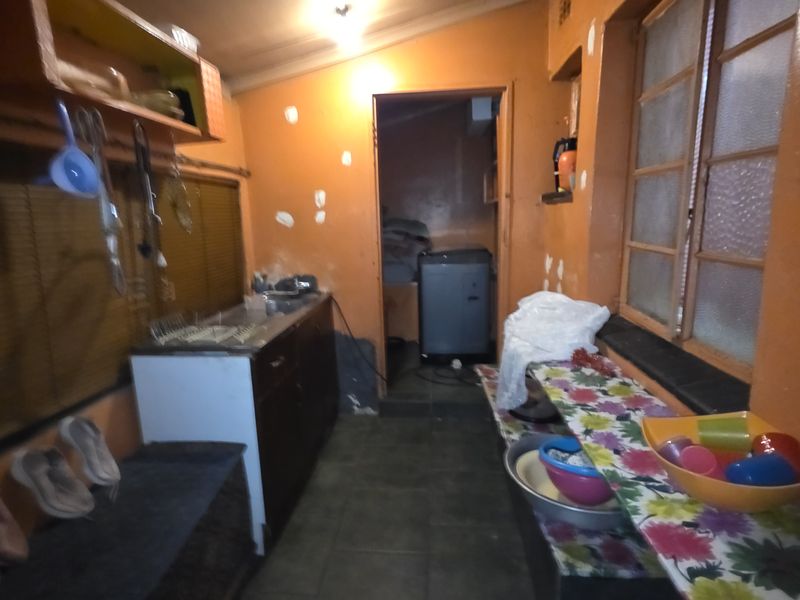 A narrow utility or scullery area featuring basic cabinetry, tiled flooring, and a window, requiring cosmetic updates and maintenance.