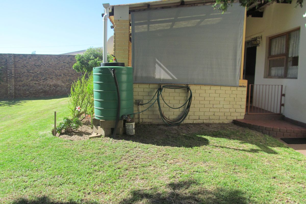 Rear garden area featuring a rainwater collection tank, covered patio space with privacy screen, and brick boundary wall.