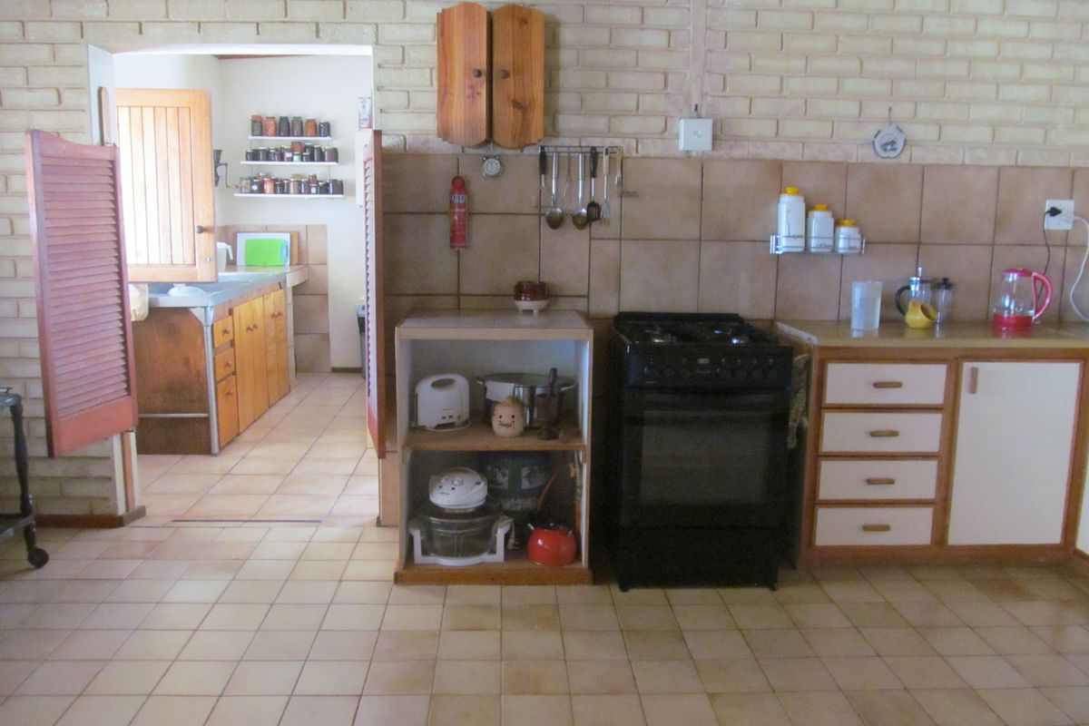 A rustic kitchen featuring exposed brick walls, tiled flooring, and a freestanding stove, with an adjacent scullery area visible through the doorway.