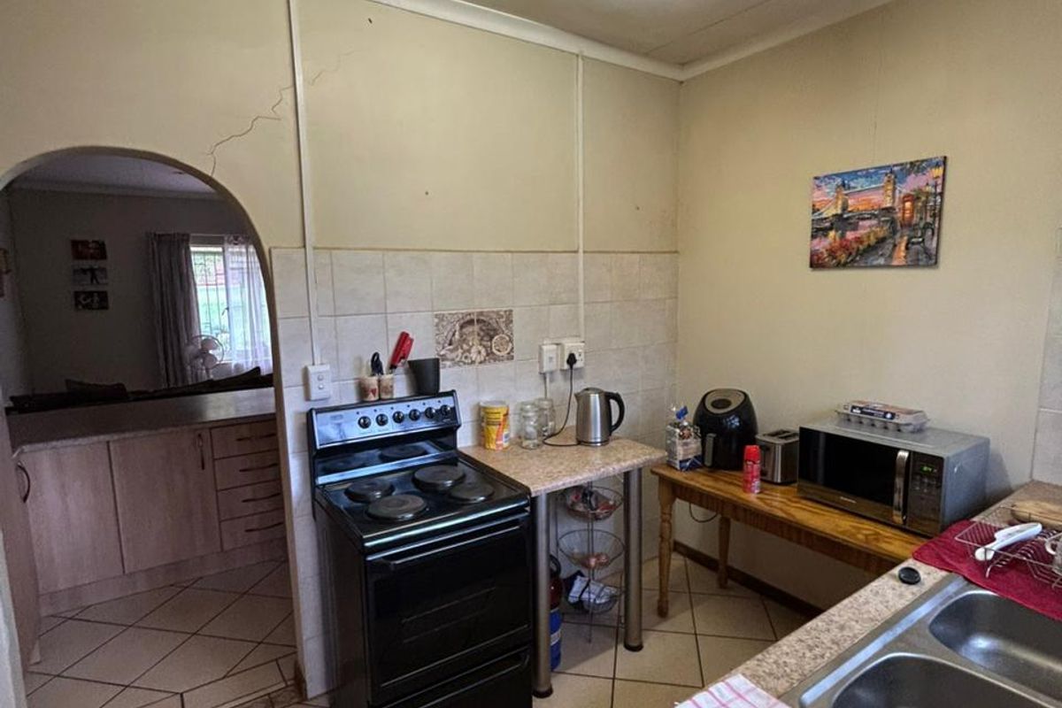 A functional kitchen featuring tiled flooring, a freestanding stove, and a double-basin sink, with an arched doorway leading to the adjacent living area.
